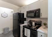 Thumbnail 3 of 47 - Kitchen view in a 1-bedroom apartment at Cambridge Court Apartments in Dallas, Texas, showing white cabinetry, black appliances, range, microwave, and pantry area.