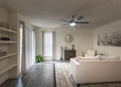 Thumbnail 17 of 47 - Living room in a 1-bedroom apartment at Cambridge Court Apartments in Dallas, Texas, showing wood-style flooring, a patio door, built-in shelving, and staged seating.
