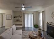 Thumbnail 18 of 47 - Living room in a 1-bedroom apartment at Cambridge Court Apartments in Dallas, Texas, showing wood-style flooring, ceiling fan, patio door, and built-in shelving.