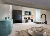 Thumbnail 16 of 47 - Breakfast bar and kitchen view in a 1-bedroom apartment at Cambridge Court Apartments in Dallas, Texas, showing counter seating, sink, black appliances, and open connection to the living area. Title: Cambridge Court Breakfast Bar and Kitchen