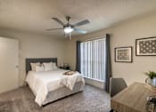 Thumbnail 21 of 47 - Bedroom in a 1-bedroom apartment at Cambridge Court Apartments in Dallas, Texas, showing carpeted flooring, ceiling fan, patio door, and staged furniture.