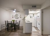 Thumbnail 1 of 40 - A kitchen with a white cabinets and appliances and the dining room with table and chairs in a 515 square foot 1 bedroom, 1 bath apartment home at Canyon Creek Apartments in Dallas Midtown neighborhood of Dallas, TX.
