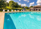 Thumbnail 57 of 82 - A pool surrounded by white lounge chairs with the playground in the background at Fairfield Pointe Apartments in Fairfield, Ohio.