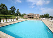 Thumbnail 67 of 74 - A large swimming pool with white lounge chairs and a building in the background.