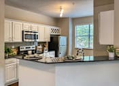 Thumbnail 6 of 52 - A kitchen with a black granite counter top and white cabinets in the 1486 square foot 3 bedroom, 3 bath apartment with attached 2-car garage at The Brownstones in Far North, Dallas, Texas