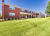 Thumbnail 53 of 59 - Brick apartment building exterior with open green lawn near the pool area at Lake of the Woods Apartments