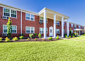 Thumbnail 55 of 59 - Apartment building exterior with white columned entry and manicured grass at Lake of the Woods Apartments