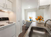 Thumbnail 14 of 34 - A kitchen with a stove, sink, and a dining table with chairs.