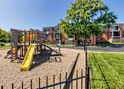 Thumbnail 49 of 60 - Playground and fenced recreation area with apartment buildings in the background at Village East Apartments
