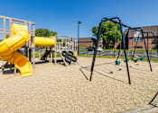Thumbnail 48 of 60 - Playground with spiral slide, swings, and open play area at Village East Apartments