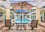 Thumbnail 4 of 19 - a patio with a pool and a table with chairs and an umbrella at Olive Tree Apartments, Torrance, CA 90503