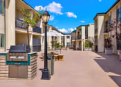 Thumbnail 11 of 36 - an outdoor patio with a grill and tables and apartments in the background at Casa Del Amo Apartments, Torrance, CA