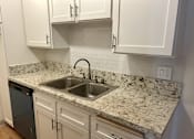 Thumbnail 36 of 36 - A kitchen with a marble countertop and white cabinets.