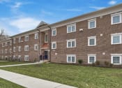 Thumbnail 13 of 15 - a brick apartment building with green grass and a sidewalk