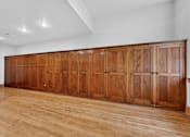 Thumbnail 20 of 50 - A long wooden cabinet with glass doors is in the middle of a room with wooden flooring.