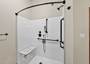 Thumbnail 24 of 50 - A white shower stall with a bench and a black shower head.