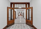 Thumbnail 50 of 50 - A hallway with a tiled floor and a row of doors on either side.