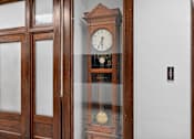 Thumbnail 48 of 50 - A wooden clock with a glass case is on a white wall.