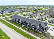 Thumbnail 26 of 28 - A large, modern apartment complex is surrounded by smaller houses and a road with cars.