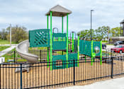 Thumbnail 25 of 28 - A playground with a green slide and a black fence.