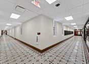 Thumbnail 47 of 50 - A long hallway with a tiled floor and an exit sign on the ceiling.