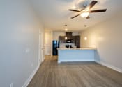 Thumbnail 35 of 65 - A room with a ceiling fan and a kitchen area in the background.