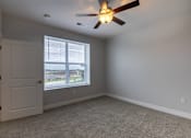 Thumbnail 38 of 65 - A room with a ceiling fan and a window overlooking a parking lot.