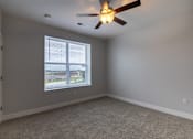 Thumbnail 32 of 65 - A room with a ceiling fan and a window overlooking a parking lot.