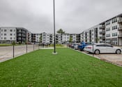 Thumbnail 55 of 65 - A grassy area in front of apartment buildings with cars parked in the background.