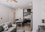 Thumbnail 13 of 22 - A modern living room with a grey couch and a kitchen area in the background.