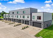 Thumbnail 29 of 34 - A modern building with grey walls and a grey roof is surrounded by a concrete driveway and a grassy area.