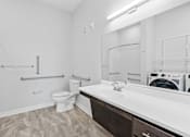 Thumbnail 36 of 52 - A white bathroom with a toilet, sink, and a washing machine in the corner.