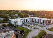Thumbnail 19 of 65 - A sunset view of a large apartment complex with a parking lot in front.