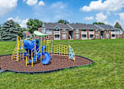 Thumbnail 44 of 53 - A playground with a blue slide and yellow safety barriers in front of a brick building.