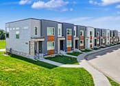 Thumbnail 9 of 36 - A row of modern townhouses with a sidewalk and green grass in front.