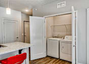 Thumbnail 23 of 31 - A small kitchen with a red chair and white cabinets.