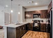 Thumbnail 2 of 31 - A kitchen with dark wood cabinets and a black refrigerator.