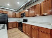 Thumbnail 27 of 35 - A kitchen with wooden cabinets and a black fridge at Melbourne Apartments, Des Moines