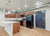 Thumbnail 23 of 35 - A kitchen with a black refrigerator and wooden cabinets at Melbourne Apartments, Des Moines, IA