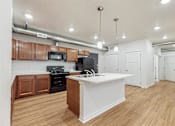 Thumbnail 24 of 35 - A kitchen with a white island and wooden cabinets at Melbourne Apartments, IA, 50320