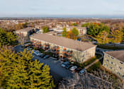 Thumbnail 53 of 90 - An aerial view of a parking lot and buildings with trees in the foreground. at Rosemont Place Apartments, Des Moines