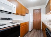 Thumbnail 27 of 90 - A kitchen with a black stove top oven, a white microwave, a white refrigerator, and wooden cabinets at Rosemont Place Apartments, Des Moines, IA