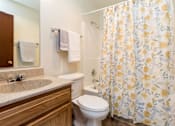 Thumbnail 12 of 26 - A bathroom with a toilet, sink, and shower curtain at Sutton Hill Apartments, Des Moines