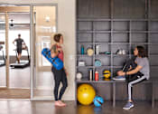 Thumbnail 27 of 40 - two women working out in a gym with weights and a yoga ball at Velocity Apartments, IA, 50309