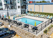 Thumbnail 20 of 40 - a swimming pool with lounge chairs in front of a building at Velocity Apartments, Des Moines, IA