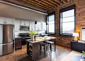 Thumbnail 45 of 99 - A kitchen with a wooden table and chairs, a refrigerator, and a brick wall.at Plant 1 Lofts, N. Newton  