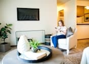 Thumbnail 2 of 57 - a woman sitting in a chair in a living room looking at her cell phone at Bristol Ridge, Urbandale