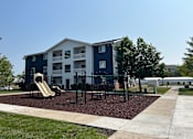 Thumbnail 1 of 7 - A playground area in front of a blue and white apartment building.