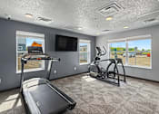 Thumbnail 33 of 53 - A spacious room with a treadmill, elliptical trainer, and a television.