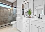 Thumbnail 7 of 36 - A bathroom with a white toilet, white sink, and tile throughout the shower.